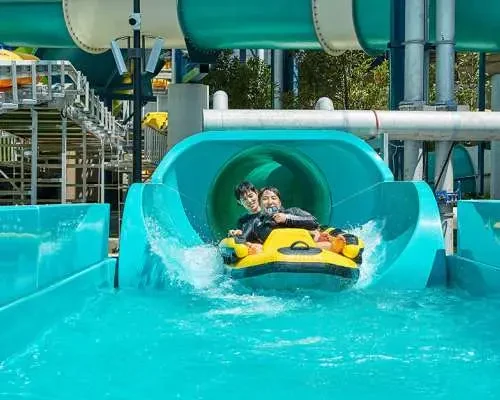 Shinhwa Water Park 遊客乘黃色充氣筏滑出藍色封閉滑水道真實照片